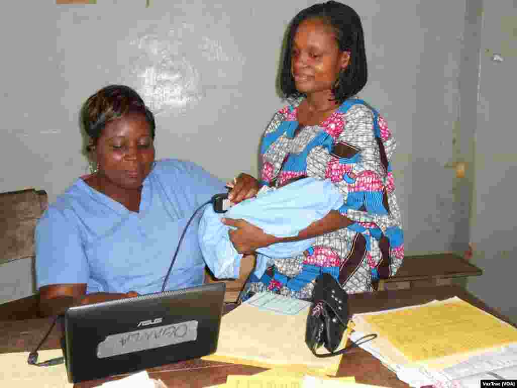 A health care worker holds a baby&rsquo;s finger on a scanning device to capture its fingerprint at a clinic in Benin. (VaxTrac) 