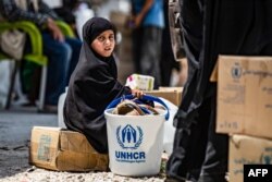 시리아 북동부 알홀 난민캠프에서 한 소녀가 유엔의 인도주의 지원 물품 옆에 앉아있다.