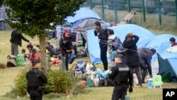 French police officers watch migrants packing their belongings in a camp of Grande Synthe, northern France, Tuesday, Sept.17, 2019.