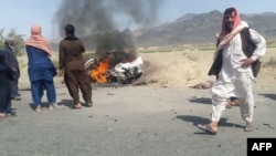 FILE - Local residents gather around a burning vehicle hit by a U.S. drone strike, May 21, 2016, near Dalbandin, Pakistan. Afghan Taliban leader Mullah Mansoor was killed in the strike. Kabul accuses Islamabad of clandestinely supporting the Afghan Taliban.