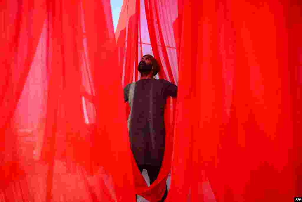 A worker hangs dyed shawls at a shop in Lahore, Pakistan.