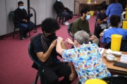 FILE - Members of the public receive a dose of the AstraZeneca/Oxford vaccine at a coronavirus vaccination center at the Fazl Mosque in southwest London, March 23, 2021.