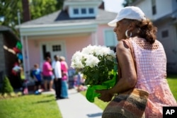 A mourner carries flowers to leave at the childhood home of Muhammad Ali, rear, June 5, 2016, in Louisville, Kentucky. The revered heavyweight champion who died Friday at the age of 74, is to be buried on June 10.