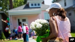 A mourner carries flowers to leave at the childhood home of Muhammad Ali, rear, June 5, 2016, in Louisville, Kentucky. The revered heavyweight champion who died Friday at the age of 74, is to be buried on June 10.
