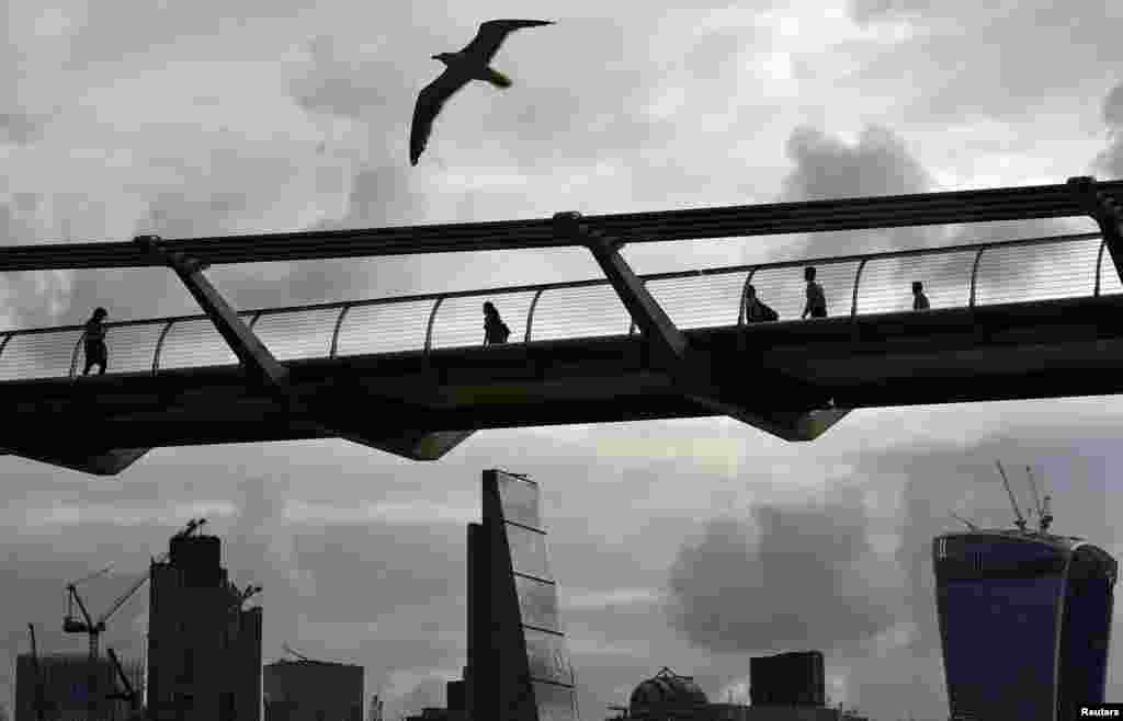 Workers cross the Millenium Bridge with the City of London in the background, Britain.