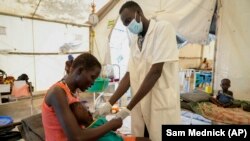 FILE: A woman's malnourished child is attended by a doctor in a hospital in Jonglei state, South Sudan Tuesday, Dec. 28, 2021. Aid groups say more will face hunger this year, because of severe floods as well as conflict and the sluggish implementation of the peace agreement.