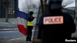 FILE - A protester wearing a yellow vest holds a French flag as the authorities dismantle their shelter at a traffic island near the A2 Paris-Brussels motorway in Fontaine-Notre-Dame, France, Dec. 14, 2018. 
