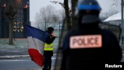 A protester wearing a yellow vest holds a French flag as the authorities dismantle their shelter at a traffic island near the A2 Paris-Brussels motorway in Fontaine-Notre-Dame, France, Dec. 14, 2018. 