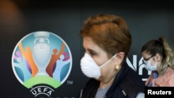 Travellers pass by a logo of the 2020 UEFA European Football Championship displayed on a wall inside Bucharest Henri Coanda International Airport, in Otopeni, Romania, March 16, 2020.