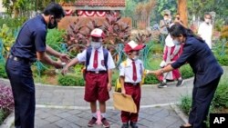 Petugas memeriksa suhu tubuh siswa sebuah SD di Jakarta, pada hari pertama sekolah dibuka kembali, 30 Agustus 2021. (AP Photo/Dita Alangkara)