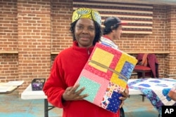 Hadijah Petro, who is originally from Congo, shows a handmade quilt she picked out for herself at a blanket giveaway for refugees and immigrants on March 21, 2023, in Burlington, Vt. Each included a note from the crafter about her or his own family history of immigration or migration. (AP Photo/Lisa Rathke)