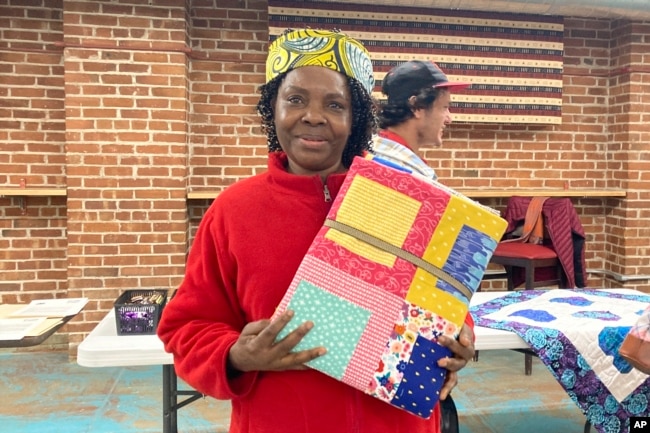 Hadijah Petro, who is originally from Congo, shows a handmade quilt she picked out for herself at a blanket giveaway for refugees and immigrants on March 21, 2023, in Burlington, Vt. Each included a note from the crafter about her or his own family history of immigration or migration. (AP Photo/Lisa Rathke)