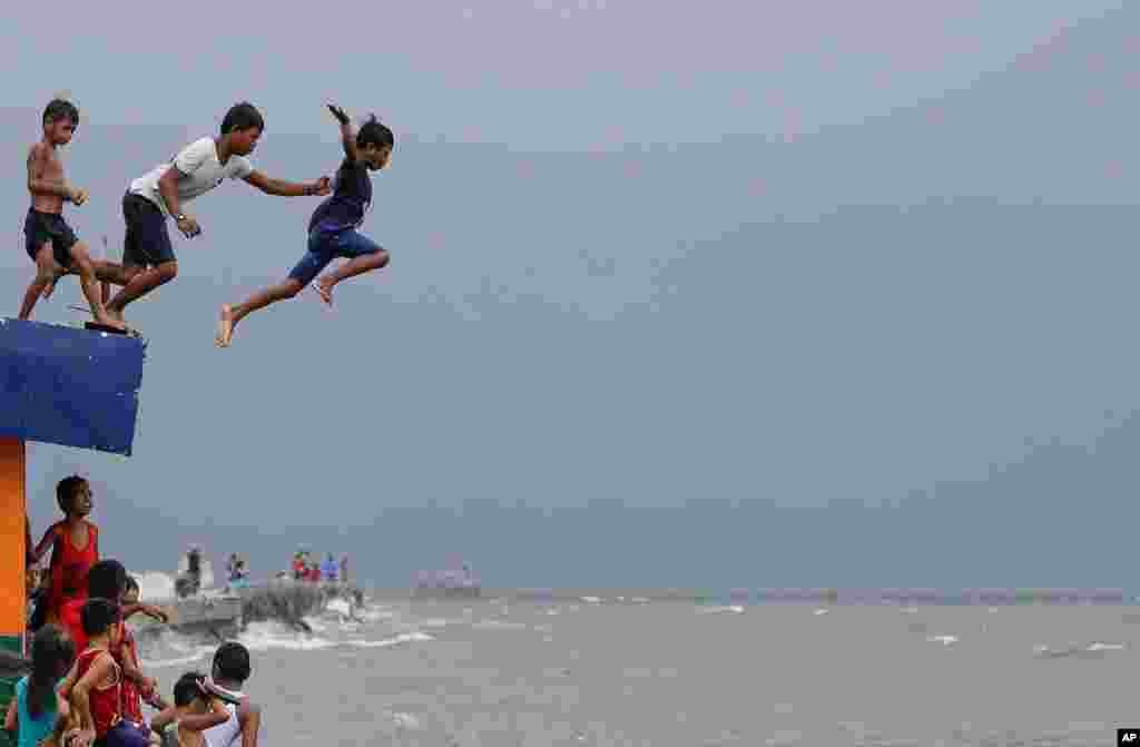 Boys jump into the water despite powerful waves after a strong downpour at Manila&#39;s Bay, Philippines.