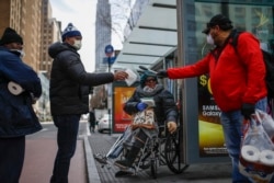 Felix Guzman, kanan, mengenakan sarung tangan pelindung dan masker membagikan sarung tangan sekali pakai duntuk orang-orang yang tak memliliki tempat tinggal di 34th Street, Sabtu, 21 Maret 2020, di New York. (Foto: AP)
