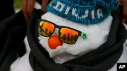 A man wraps a scarf on a snowman decked out with sunglasses, a knitted cap and an orange serving as a nose, as others play in a snow-covered park in Santiago, Chile, July 15, 2017. 