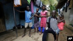 FILE - Laboratory technician Mohamed SK Sesay, who survived Ebola but saw many of his colleagues die and now has joint and muscle pains and loss of sight, holds the child of one of his work colleagues who died of the disease, in Kenema, Sierra Leone, Aug. 9, 2015.