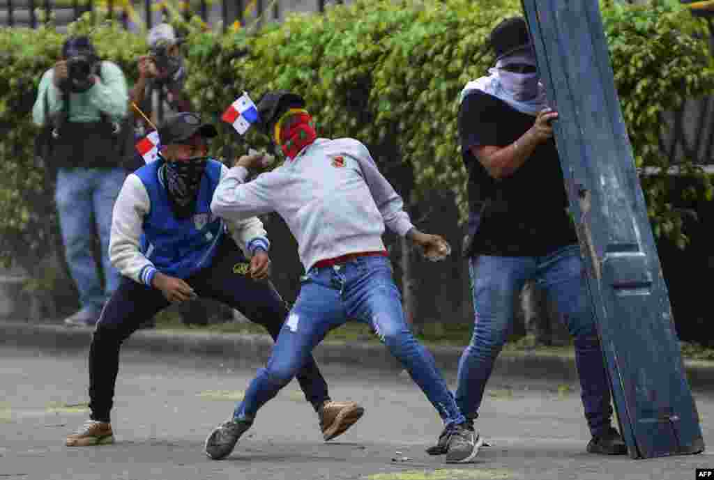 Un manifestante se refugia detrás de una puerta mientras otro arroja una piedra durante un enfrentamiento con la policía antidisturbios.