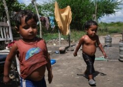 FILE - Pastor, 3, and Josue, 4, both of whom have been hospitalized in the past for malnutrition according to their mother Gregoria Hernandez, walk outside their house in Barquisimeto, Venezuela, Nov. 28, 2019.