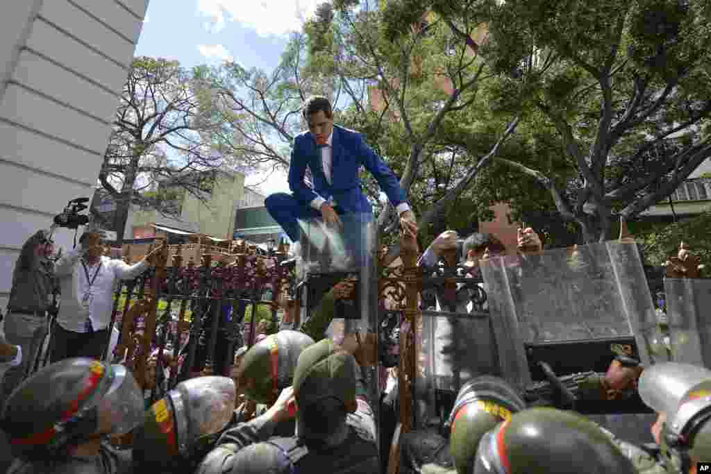 Venezuela’s National Assembly President and opposition leader Juan Guaido tries to climb the fence to enter the compound of the Assembly in Caracas, after he and other opposition lawmakers were blocked by police, Jan. 5, 2020.