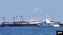 FILE - This handout video grab taken on April 27, 2021, and received from the Philippine Coast Guard on May 5, 2021, shows the Philippine Coast Guard ship BRP Cabra (front) monitoring Chinese vessels at Sabina Shoal, a South China Sea outcrop claimed by Manila.