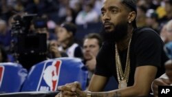 FILE - Rapper Nipsey Hussle watches an NBA basketball game between the Golden State Warriors and the Milwaukee Bucks, March 29, 2018, in Oakland, Calif. 