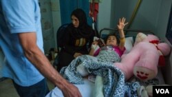 Sara, 8, cries as her father looks at her one broken leg — the other has been severed — in Qamishli, Syria, Oct. 15, 2019. (Y. Boechat/VOA)