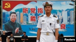 在香港海軍基地，一位中國水兵站在一面具有中共黨旗、習近平像和香港景象的大型看板前面（2017年7月8日）。