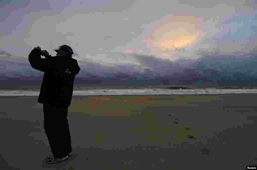 A man takes a picture of calm seas and sun-dappled clouds in the aftermath of Hurricane Sandy, at sunrise on Rehoboth Beach, Delaware Oct. 30, 2012. 