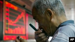 A Chinese investor uses a magnifying glass to look at his mobile phone screen as he monitors stock prices at a brokerage house in Beijing, China, July 9, 2015. 