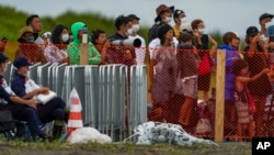 People watch from behind a security fence during the final day of the surfing competition at the 2020 Summer Olympics, Tuesday, July 27, 2021, at Tsurigasaki beach in Ichinomiya, Japan. (AP Photo/Francisco Seco)