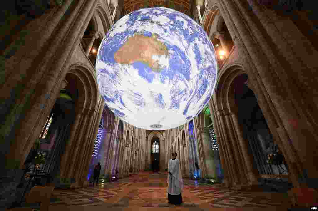 A member of the clergy poses under British artist Luke Jerram&#39;s installation &#39;Gaia&#39;, a 7-meter replica of planet Earth, suspended in the nave of Ely Cathedral in Ely, Cambridgeshire, Britain.