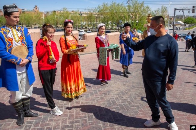 FILE - A tourist snaps pictures of Uyghur performers at the front gate of the remodeled city center of Kashgar in China's far west Xinjiang region, during the welcome ceremony of a state tour for foreign media, April 19, 2021.