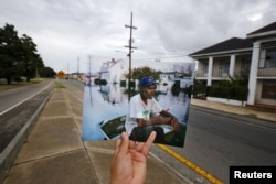 FILE - Photographer Carlos Barria holds a print of a photograph he took in 2005, as he matches it up at the same location 10 years on, in New Orleans, Aug. 16, 2015.
