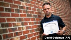 In this March 11, 2016 photo, Shane Satterfield, a roofer who owes more than $30,000 in debt for a two-year degree in computer science from one of the country’s largest for-profit college companies that failed in 2014, holds his diploma in Atlanta.