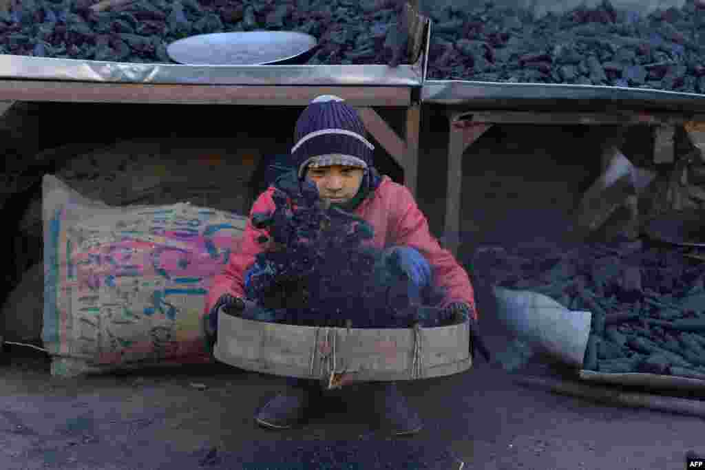 A young Afghan vendor sifts charcoal at his stall in Herat city.