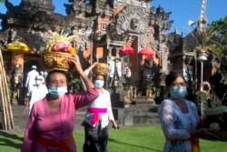 Orang-orang yang memakai masker sebagai tindakan pencegahan penyebaran virus corona membawa sesaji selama festival Hindu Galungan, di sebuah pura di Bali, pada Rabu, 14 April 2021. (Foto: AP)
