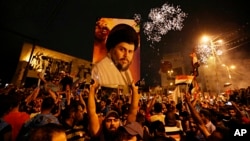 FILE - Followers of Shiite cleric Muqtada al-Sadr, seen pictured on the poster, celebrate in Tahrir Square, Baghdad, Iraq, May 14, 2018.