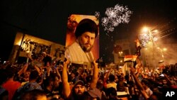 Followers of Shi'ite cleric Muqtada al-Sadr, seen pictured on the poster, celebrate in Tahrir Square, Baghdad, Iraq, early Monday, May 14, 2018.
