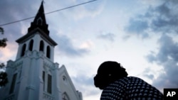 FILE - A woman stands next to Emanuel AME Church, the site of the mass shooting, as the sun rises, June 26, 2015, in Charleston. 