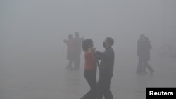 FILE - People wearing masks dance at a square in heavy smog during a polluted day in Fuyang, Anhui province, China, Jan. 3, 2017. Beijing is concerned that the spread of unauthorized or inaccurate pollution data from popular mobile apps and handheld detectors.