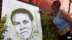 A woman signs a mural of boxing great Muhammad Ali in the Brooklyn Borough of New York outside of a gathering hosted by director Spike Lee, June 4, 2016. 