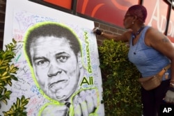 A woman signs a mural of boxing great Muhammad Ali in the Brooklyn Borough of New York outside of a gathering hosted by director Spike Lee, June 4, 2016.