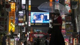 Pedestrians walk past a giant public TV with a live broadcast of a news conference by Japanese Prime Minister Yoshihide Suga after he announced a state of emergency because of rising coronavirus infections Thursday, July 8, 2021, in Tokyo.
