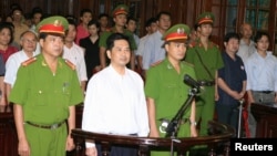 Cu Huy Ha Vu (C) stands between policemen in the dock during his trial at a court in Hanoi, August 21, 2011.