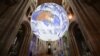 A member of the clergy poses under British artist Luke Jerram's installation 'Gaia', a 7 meter replica of planet Earth, suspended in the nave of Ely Cathedral in Ely, Cambridgeshire, on June 30, 2021.