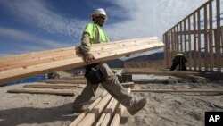 Construction worker Miguel Fonseca carries lumber as he works on a house frame for a new home, Nov. 16, 2012, in Chula Vista, California.