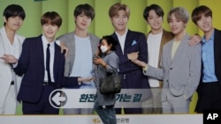 A woman wearing a face mask to help protect against the spread of the coronavirus walks by a board showing members of South Korean K-Pop group BTS to advertise a local bank's money exchange in Seoul, South Korea, Sept. 30, 2020. 