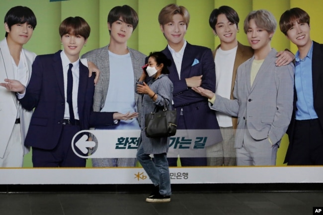 A woman wearing a face mask to help protect against the spread of the coronavirus walks by a board showing members of South Korean K-Pop group BTS in Seoul, South Korea, Wednesday, Sept. 30, 2020. (AP Photo)