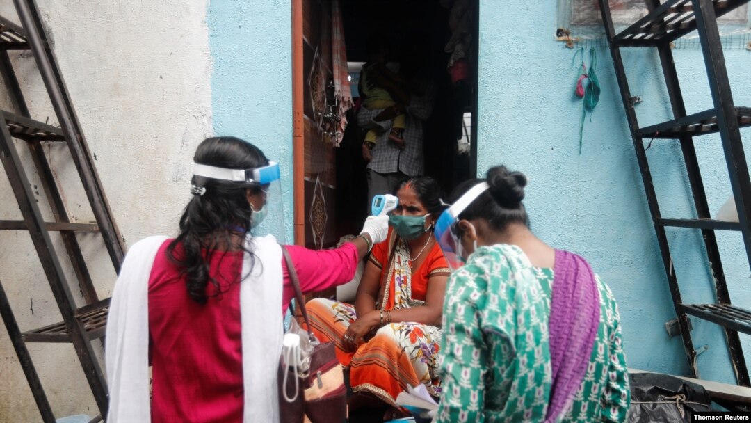 Voluntarios comunitarios de salud controlan la temperatura de una mujer durante una campaña de control de la COVID-19, en un barrio pobre de Mumbai, India, el 16 de agosto de 2020.