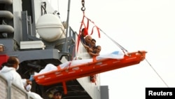 Armed Forces of Malta sailors watch the body of a drowned migrant being lowered from their ship after arriving at the AFM Maritime Squadron base in Valletta's Marsamxett Harbor, Oct. 12, 2013. 